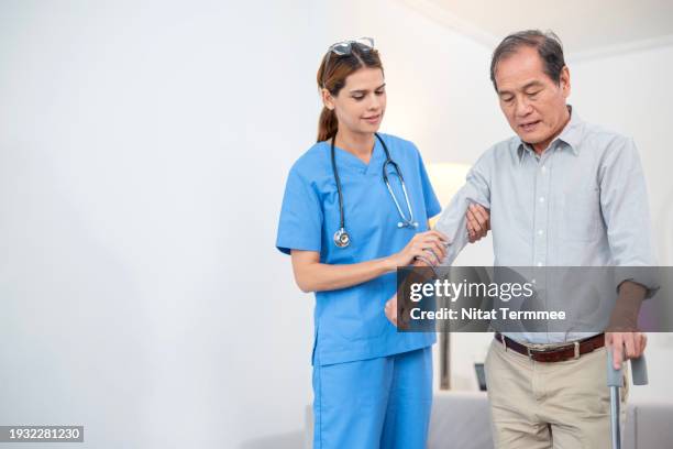 in-home physical therapy services to improve a senior’s range of motion and reduce the chances of a future injury. a caring female physical therapist helps stroke victims walk with a walking stick during physical therapy sessions. - myasthenia gravis stock pictures, royalty-free photos & images