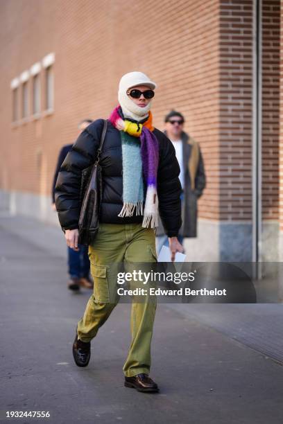 Guest wears a white balaclava, a rainbow color scarf, a black puffer oversized jacket, green cargo pants, leather shoes, a large leather bag,...