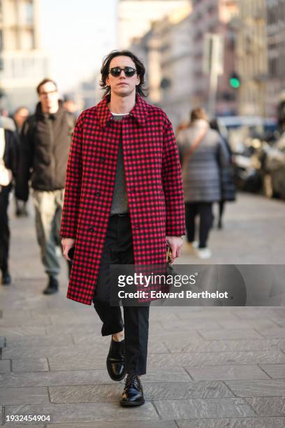 Guest wears sunglasses, a black and red checked coat, a gray pullover, suit pants, leather loafers shoes, outside MSGM, during the Milan Fashion Week...