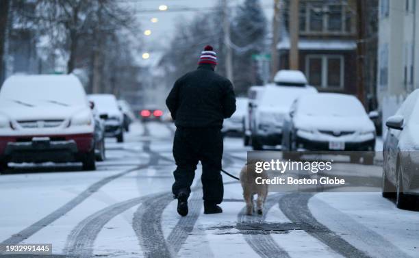 Boston, MA A man walks his dog down a snow-covered street.