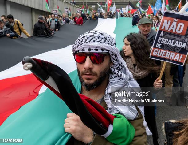 Demonstrator wearing a keffiyeh holds a large Palestinian flag while marching from the U.S Embassy to Israeli Embassy during a protest "for peace in...