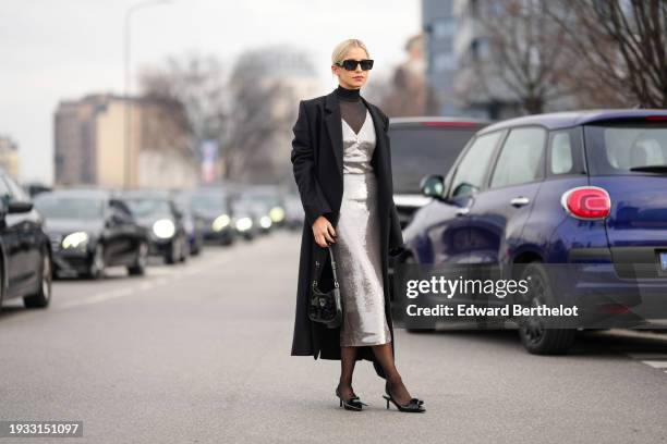 Caroline Daur wears sunglasses, a black long coat, a black turtleneck mesh top, a silver shiny sequined low neck midi dress long dress, black tights,...