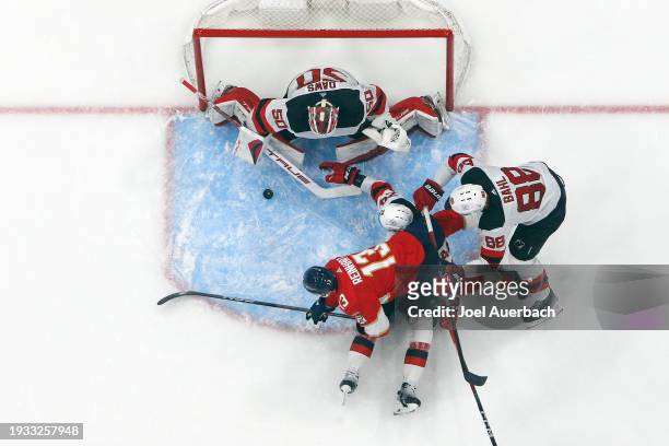 Kevin Bahl of the New Jersey Devils checks Sam Reinhart of the Florida Panthers as goaltender Nicolas Daws stops his shot at the Amerant Bank Arena...