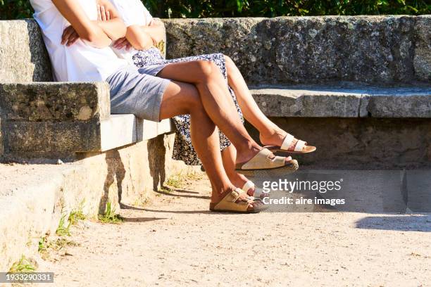 side view of the legs of a couple in casual clothes sitting on a park bench wearing sandals - vigo stock pictures, royalty-free photos & images