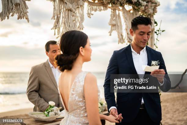 groom speaking vows to his bride in the wedding ceremony on the beach - promesas de matrimonio fotografías e imágenes de stock