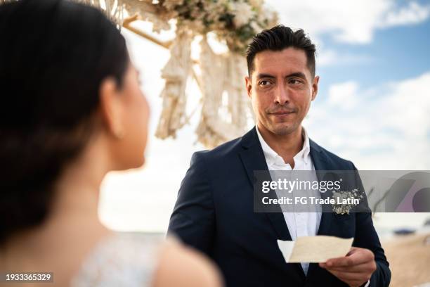 groom speaking vows to his bride in the wedding ceremony on the beach - wedding vows stock pictures, royalty-free photos & images