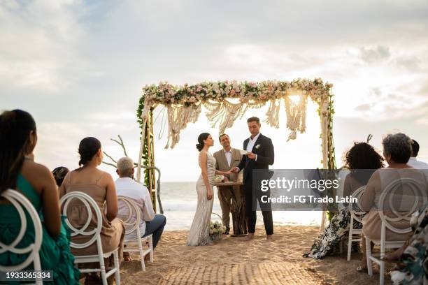 groom speaking vows to his bride in the wedding ceremony on the beach - promesas de matrimonio fotografías e imágenes de stock