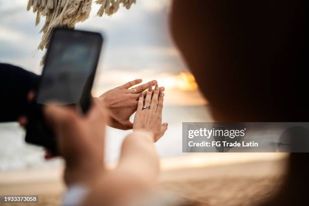 bride and groom taking a photo of their wedding rings on the beach - engagement stock pictures, royalty-free photos & images