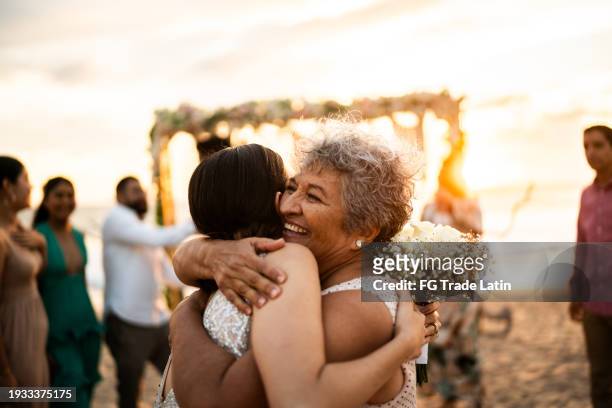 bride embracing her grandmother after wedding ceremony on the beach - milestone stockfoto's en -beelden