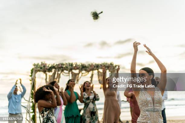 bride throwing the bouquet to her friends on the beach wedding party - bouquet toss stock pictures, royalty-free photos & images