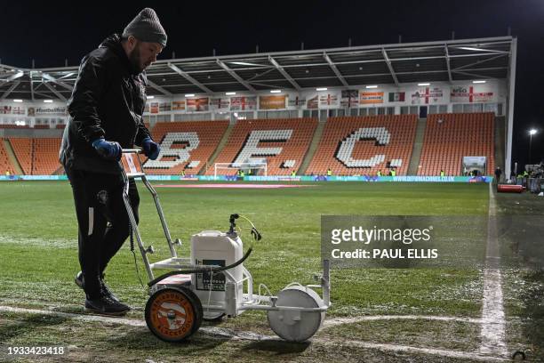 Member of the ground staff paints the white lines of the football pitch after the grass was defrosted prior to the English FA Cup third round replay...