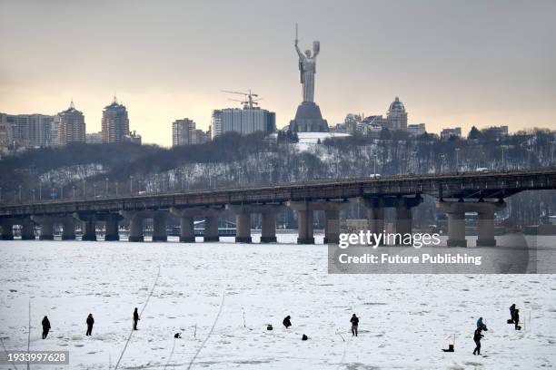 People fish on the frozen Dnipro River against the backdrop of the Motherland Monument in winter, Kyiv.