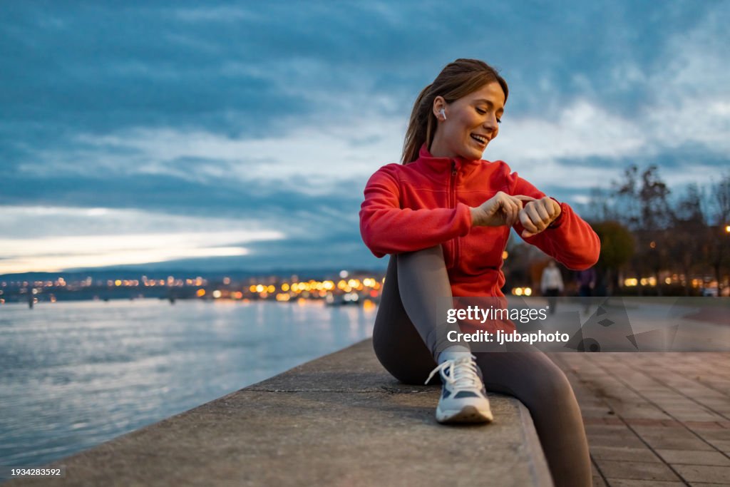 Femme athlétique heureuse en vêtements de sport regardant sa smartwatch à l’extérieur.