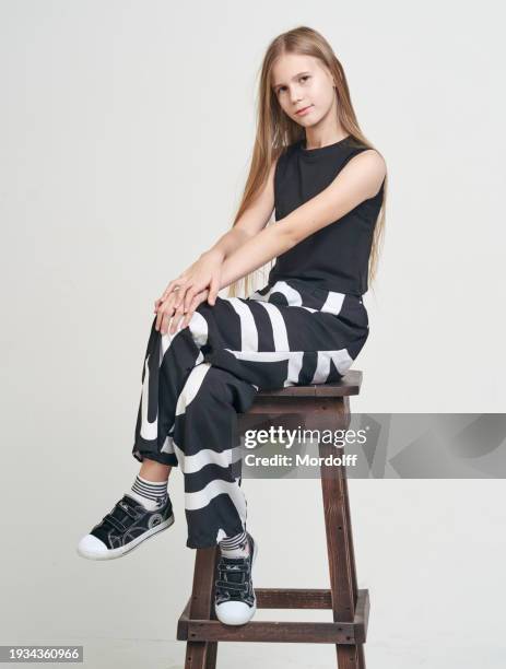 ritratto di ragazza adolescente carina dai capelli lunghi. lei è seduta con le mani sulle ginocchia, sorridente e guardando la telecamera, sfondo bianco - caucasian 11 12 girl portrait vertical beautiful foto e immagini stock