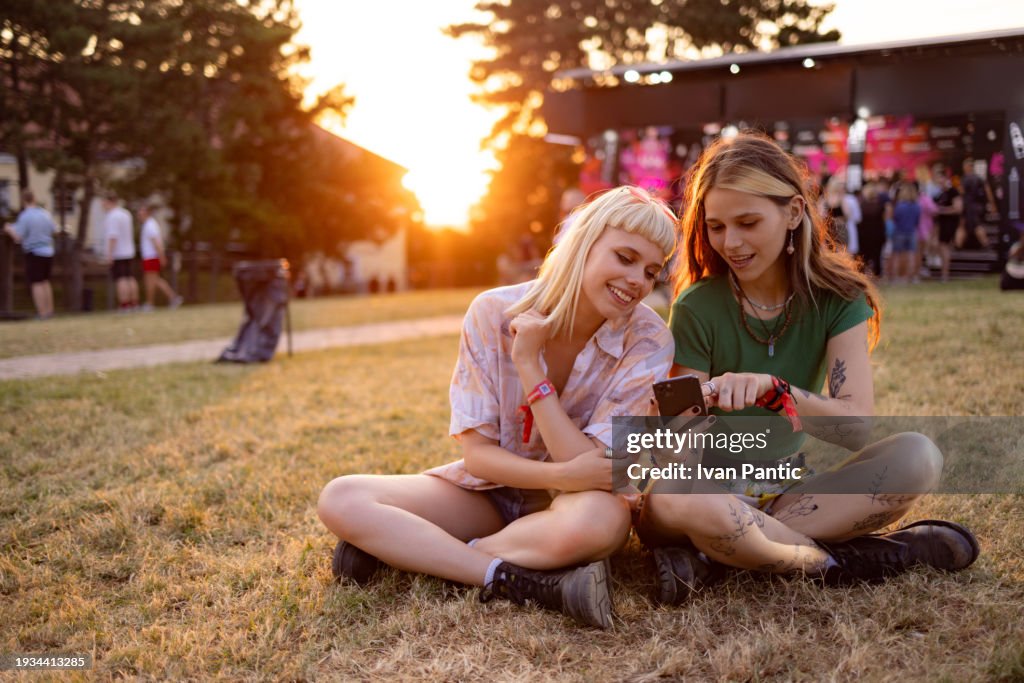 Happy female festival goers using mobile phone at sunset.