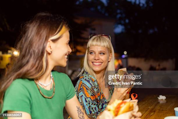 happy woman eating and talking to her friend on a music festival by night. - cuisine de rue photos et images de collection