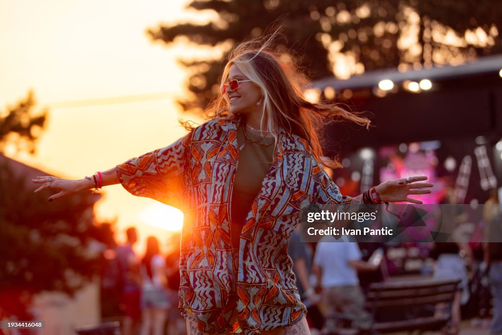 Donna felice che si diverte mentre balla in un festival musicale all'aperto al tramonto.