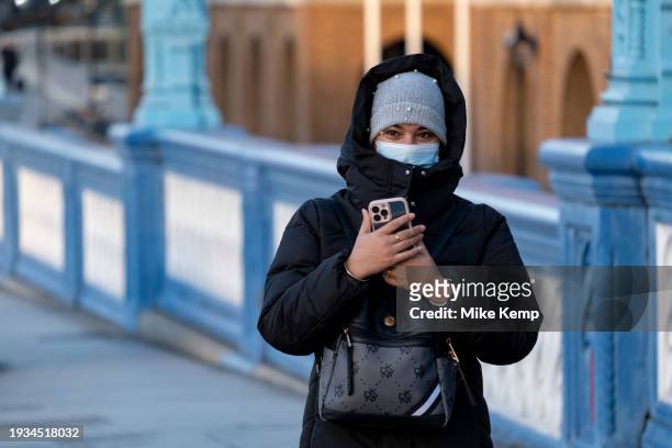 Young woman wearing a face mask to protect against Coronavirus / Covid-19 taking pictures on her smartphone as she crosses Tower Bridge on 16th...