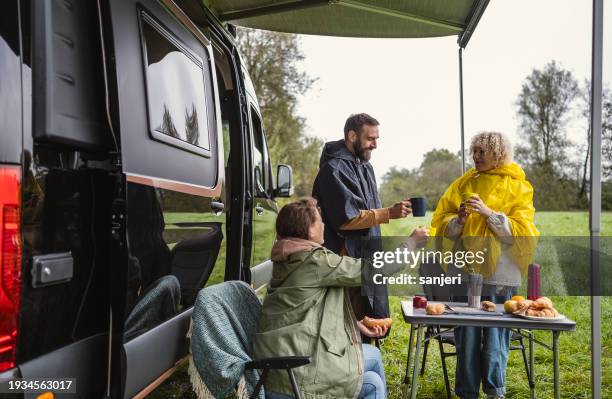 friends having fun while camping with a van - rain coat stock pictures, royalty-free photos & images