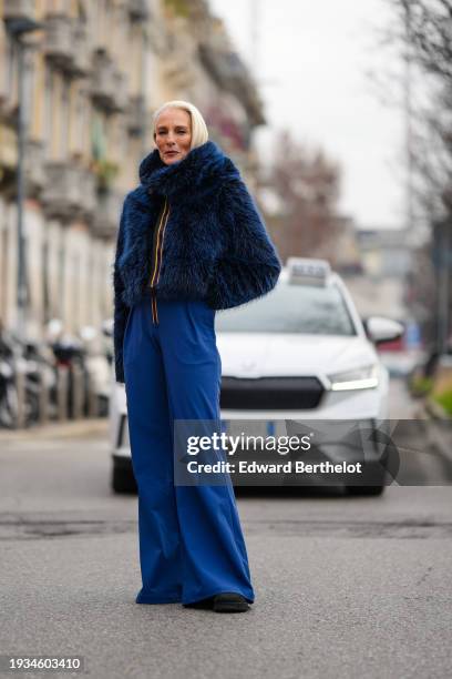 Guest wears a blue fluffy faux fur hoodie winter coat, blue flared pants, outside K-WAY, during the Milan Fashion Week - Menswear Fall/Winter...