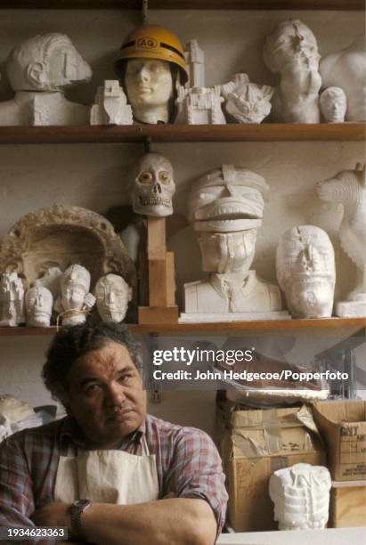 Scottish artist and sculptor Eduardo Paolozzi posed in front of various cast heads in his studio work place in Chelsea, London in 1989.