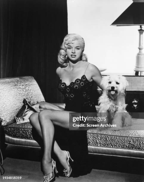 Diana Dors poses in negligee on bed with pet dog circa 1958.