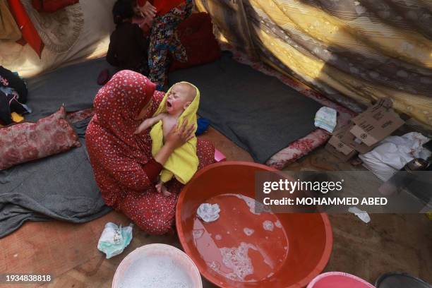 Woman dries a baby in a towel after giving it a bath, inside a tent at a camp for displaced Palestinians in Rafah in the southern Gaza Strip on...