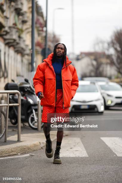 Guest wears a blue turtleneck pullover, an orange bomber jacket, orange shorts, brown boots, socks, outside K-WAY, during the Milan Fashion Week -...