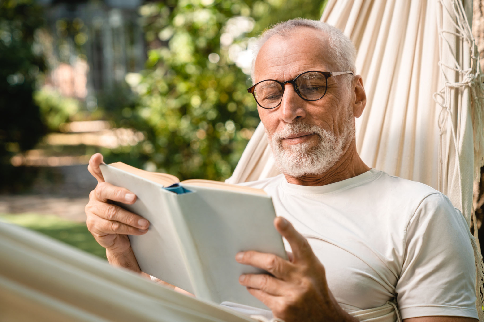 Concentrated grandfather man relaxing resting in hammock while reading book Concentrated grandfather man relaxing resting in hammock while reading book