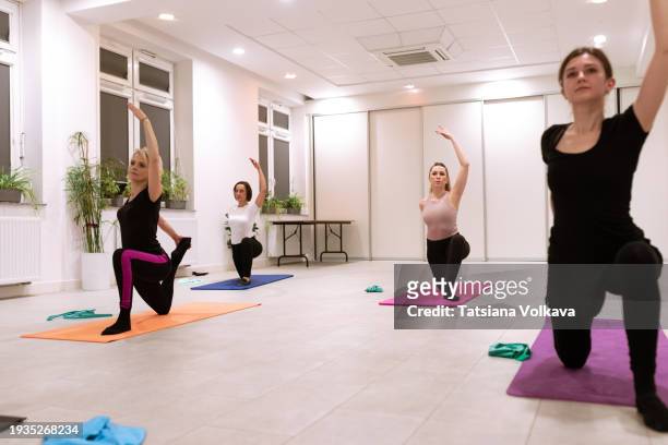 within ambiance of studio, group of ballerinas kneeling on knee of one leg, placing second bent foot on floor in front and raising one arm, engaging in lunging hip flexor stretch on mats. - ambiance girly stock pictures, royalty-free photos & images