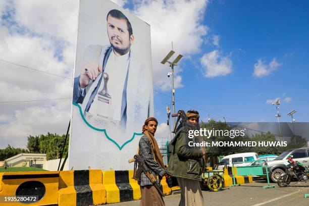 Yemeni fighters walk past a large portrait of Huthi leader Abdulmalik al-Huthi on a street in Sanaa on January 18, 2024. United States carried out...