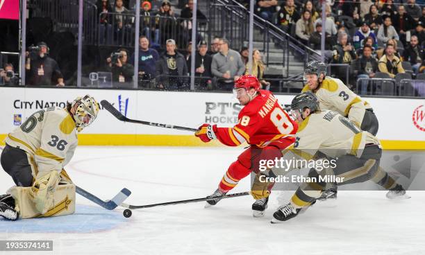 Andrew Mangiapane of the Calgary Flames attempts a shot against Logan Thompson of the Vegas Golden Knights under pressure from Kaedan Korczak and...