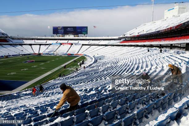 People clear snow from bleacher seats before the game between the Pittsburgh Steelers and the Buffalo Bills at Highmark Stadium on January 15, 2024...