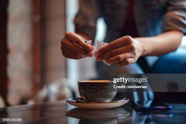donna anonima che mette lo zucchero in una tazza di caffè alla mensa - bustina foto e immagini stock