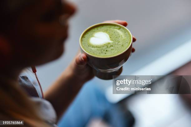 anonymous young woman enjoys drinking delicious matcha tea with green foam - matcha stockfoto's en -beelden