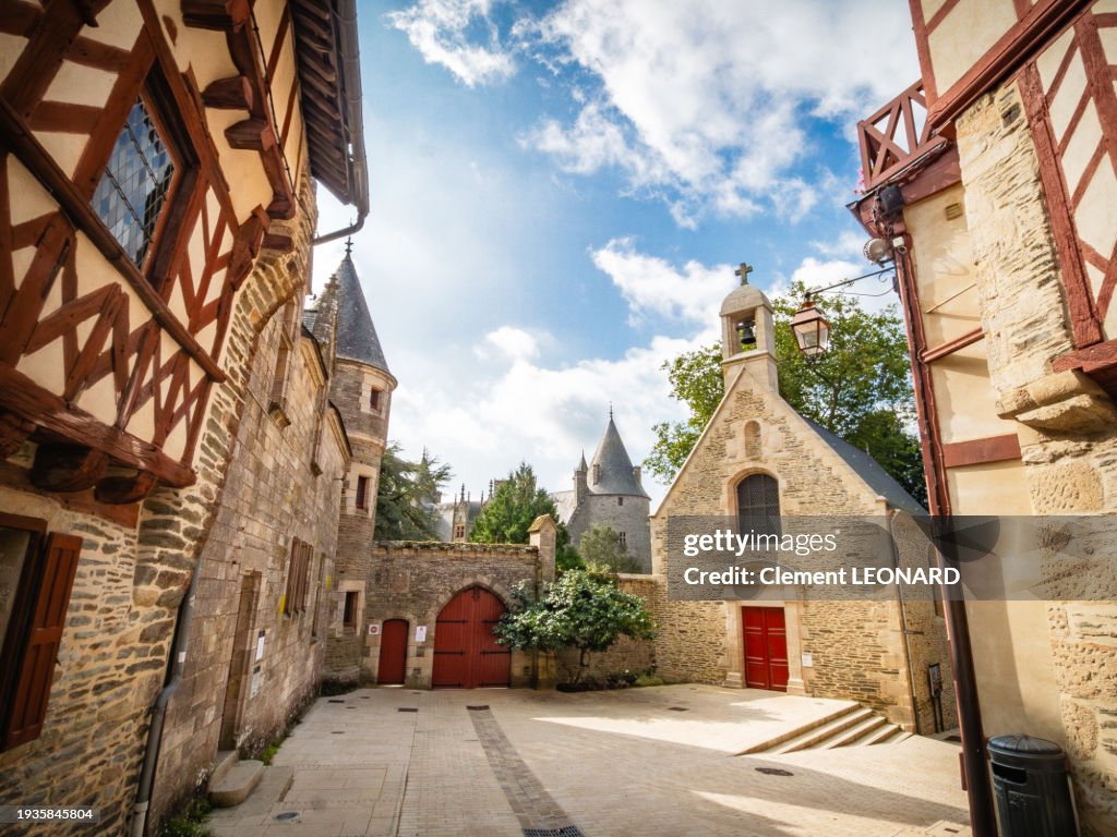 Wide angle view of a small square in the medieval old town of Josselin with half-timbered houses, a small church and a gate leading to the entrance of the gardens of the Rohan castle, Morbihan, Bretagne (Brittany), Western France.