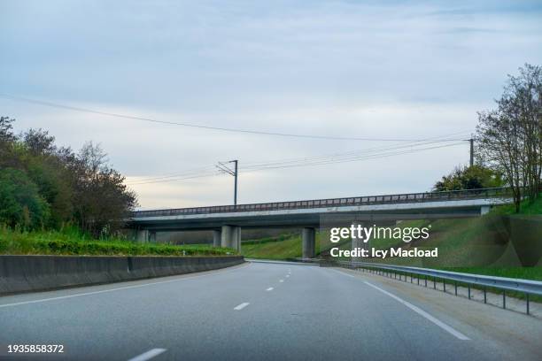the main focus is on an empty, two-lane highway road that curves slightly to the left and pass under a bridge - meerdere baans snelweg stockfoto's en -beelden