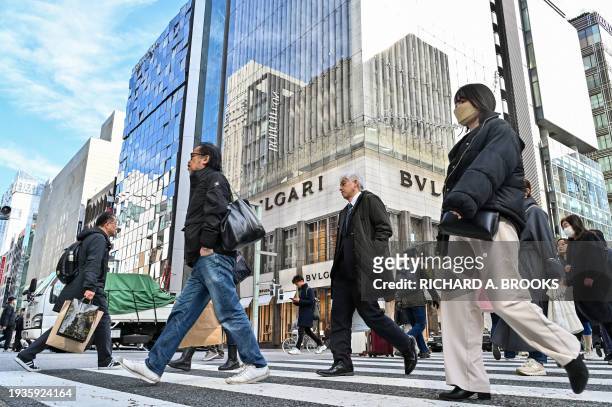Pedestrians cross the street in front of luxury shops in the Ginza shopping district in Tokyo on January 19, 2024. Japanese consumer inflation slowed...