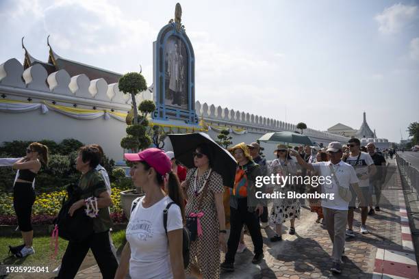 Tourists walk past a portrait of the late Thai King Bhumibol Adulyadej along the wall of the Grand Palace in Bangkok, Thailand, on Wednesday, Jan....