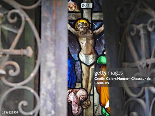 the crucifixion of jesus on an old colored stained glass and seen in the opening between two patinated metal doors. close-up of an abandoned chapel at the pere lachaise cemetery in paris, france. sunlight. natural colors. - stained glass door stock pictures, royalty-free photos & images