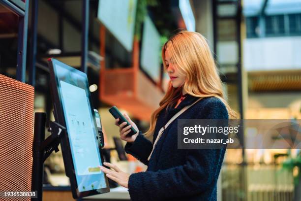 woman at cashier counter uses smartphone for payment. - automatic payment stock pictures, royalty-free photos & images