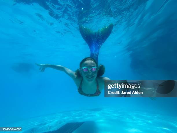 girl mermaid in blue swimming pool underwater smiling wearing bright goggles with arms outstretched with mermaid tail sticking straight up towards water’s surface - mermaid tail stock pictures, royalty-free photos & images