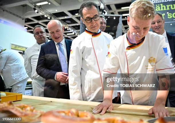Berlin's Mayor Kai Wegner and German Agriculture Minister Cem Oezdemir observe a baker preparing a pretzel at the booth of the German bakers' guild...