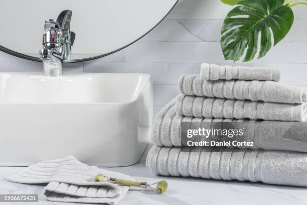 stacked folded gray towels in front of a white sink in a bathroom - counter surface level stock pictures, royalty-free photos & images