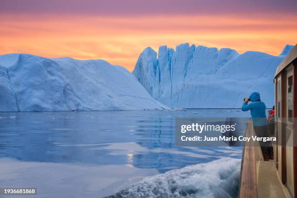 travel adventure in arctic landscape nature with icebergs, tourist man explorer from a boat looking at view of greenland icefjord at sunset - fjord stock pictures, royalty-free photos & images