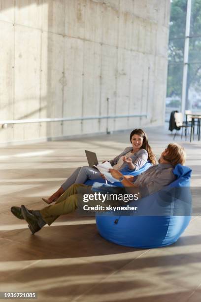 happy business colleagues talking while working on computer and paperwork at casual office. - bean bag stock pictures, royalty-free photos & images