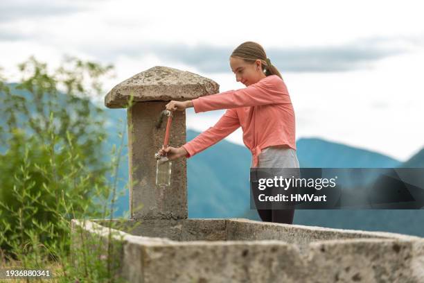 girl on mountain meadow pouring spring water from alpine water trough in glass bottle - trough stock pictures, royalty-free photos & images