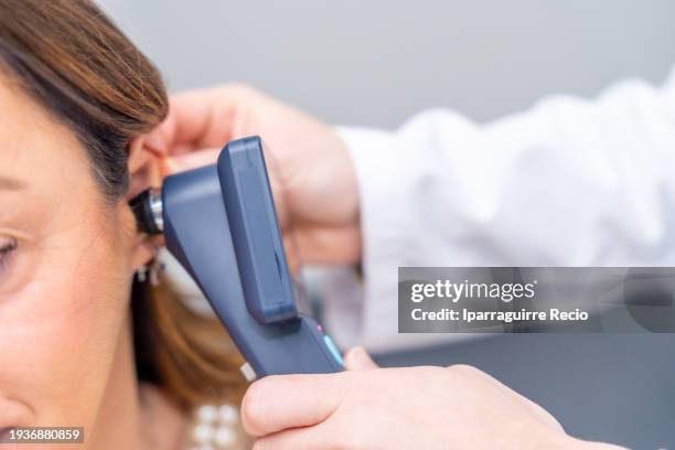 female doctor examines the patient's ear with an otoscope - ear listening stock pictures, royalty-free photos & images