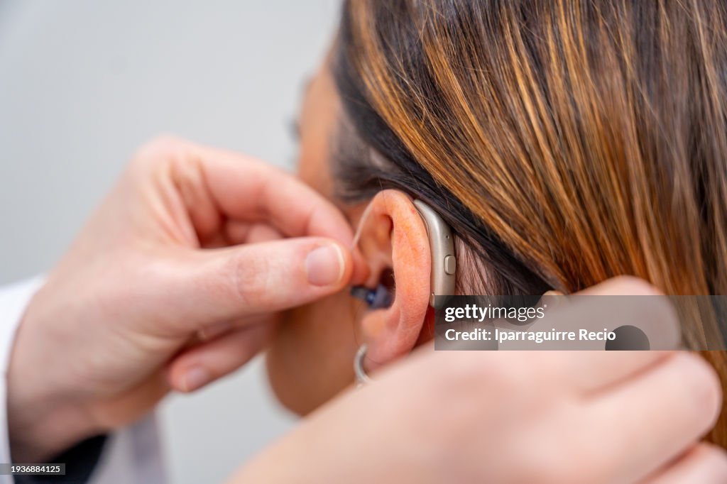 Doctor placing hearing aid to the ear of a woman