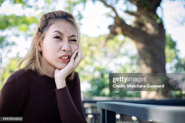 teen woman pressing her bruised cheek with a painful expression as if she is having a terrible tooth ache - gingivitis stock-fotos und bilder